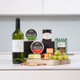 White Wine & Cheese Gift Box. A wooden serving board holds various cheeses, grapes, and crackers. Behind it are two rounds of Carrigaline cheese, a jar of chutney, and a box of Sheridan's Crackers. A bottle of white wine stands beside the food arrangement on a kitchen countertop. White Wine & Cheese Gift Box. A wooden serving board holds various cheeses, grapes, and crackers. Behind it are two rounds of Carrigaline cheese, a jar of chutney, and a box of Sheridan's Crackers. A bottle of white wine stands beside the food arrangement on a kitchen countertop.